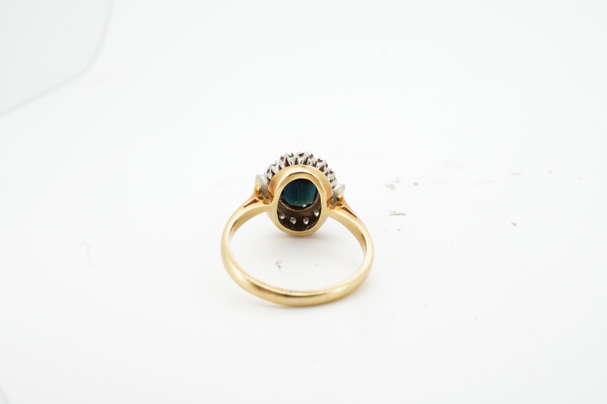 A sapphire and diamond cluster ring, claw-set with an oval sapphire measuring approximately 8.2 x 6.1 x 4.3mm, within a border of brilliant-cut and baguette diamonds totalling approximately 0.20 carats, mounted in 18ct g